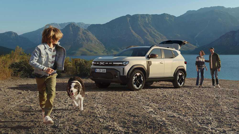 Kind und Hund laufen und blicken auf Dacia Duster am See
