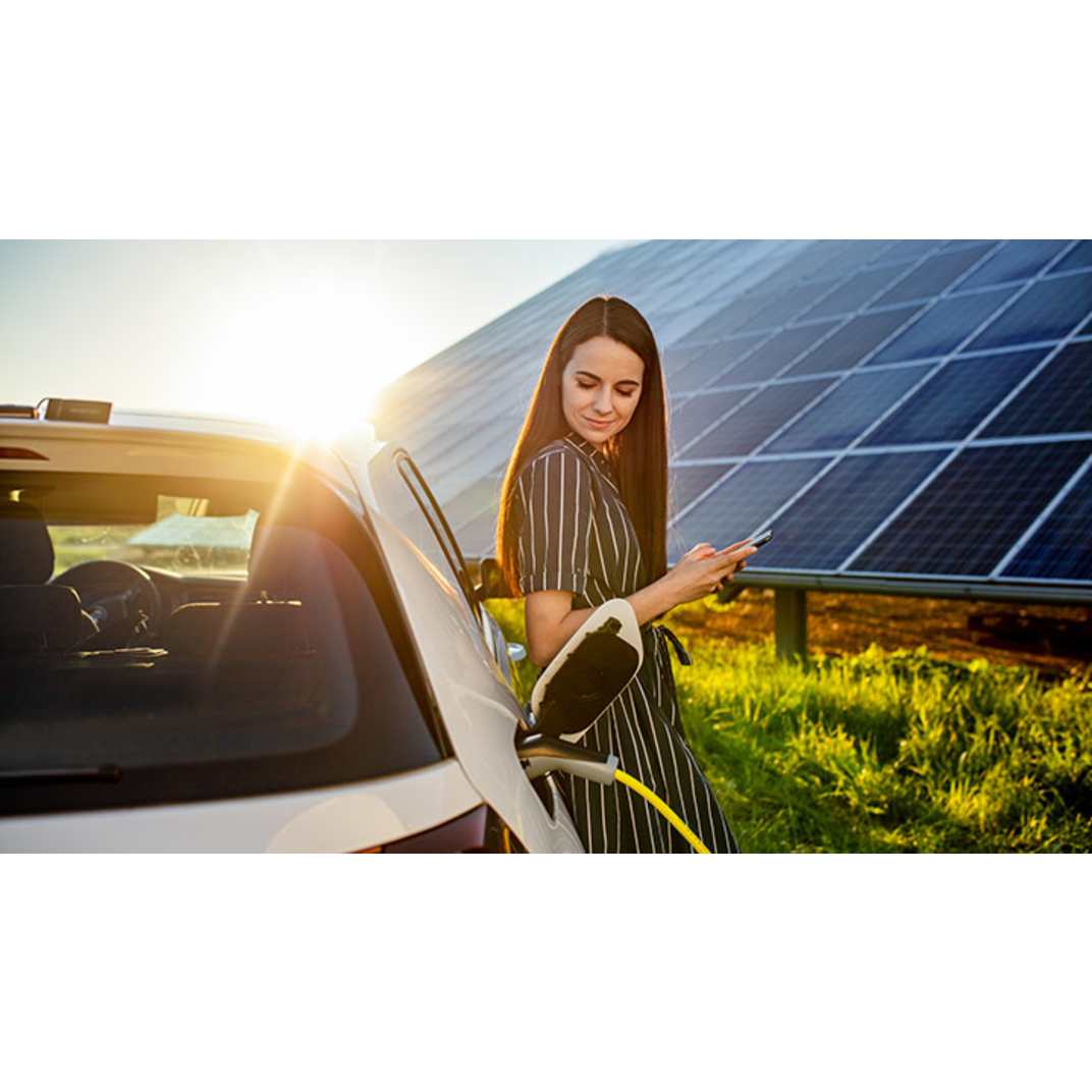 Frau lädt ihr E-Auto mit PV Anlage im Hintergrund
