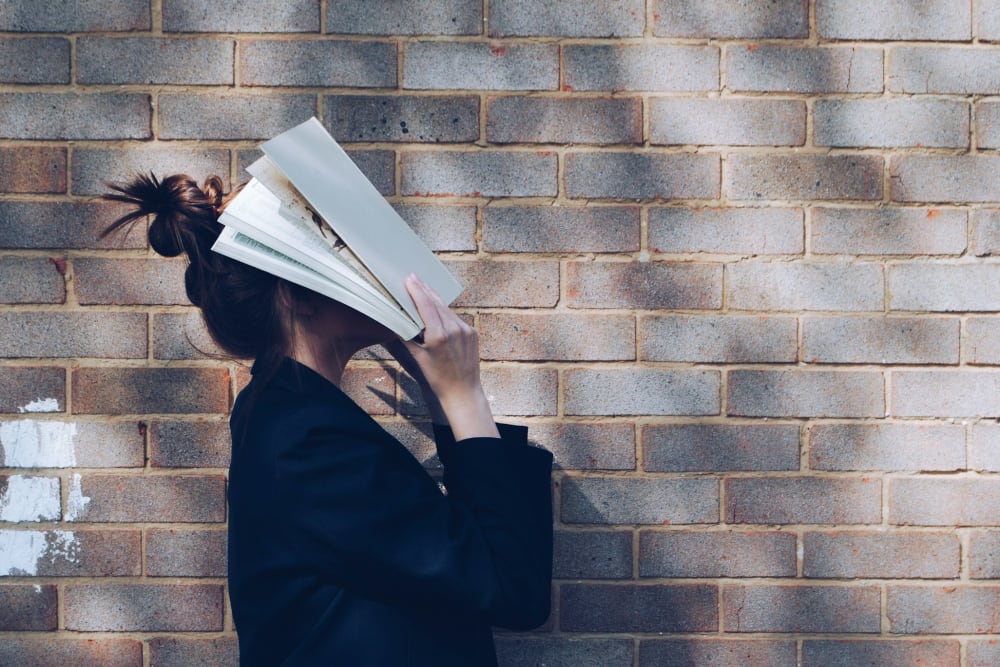 Frau mit Buch vor Wand stehend