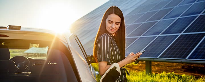 Frau lädt ihr E-Auto mit PV Anlage im Hintergrund