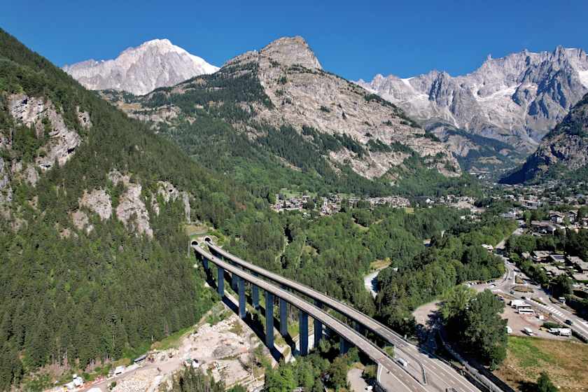 Autobahn‑Viadukt in den italienischen Alpen mit Bergen, Tal und Ortschaften im Bereich einer Mautstrecke.