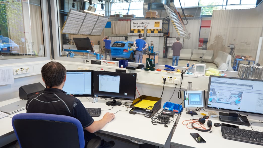 Blick über Computerbildschirme in die Crashhalle im Testzentrum in Landsberg. Vorbereitungen für den Crashtest Gepäcksicherung laufen.