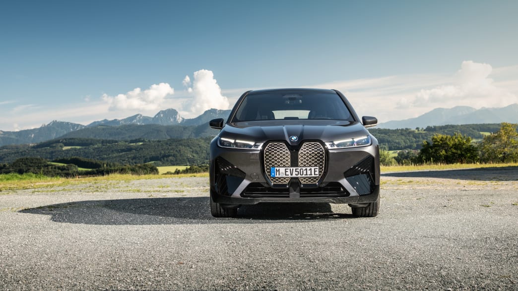 Der erste BMW iX in schwarz von vorn, parkend vor einer Bergkulisse