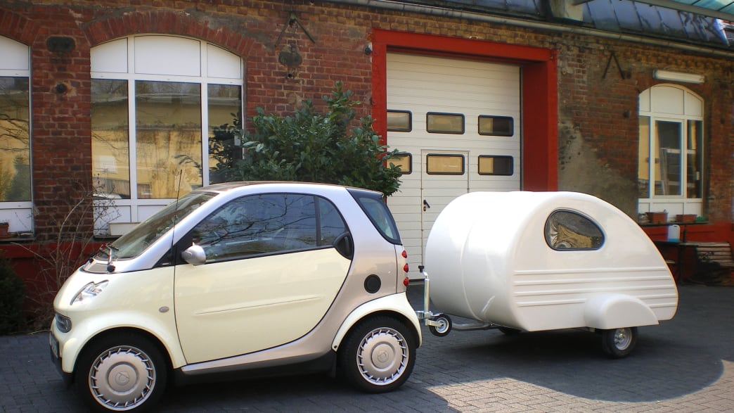 Der kleine Wohnwagen Piccolino der Firma Roehnert an einem weißen Smart