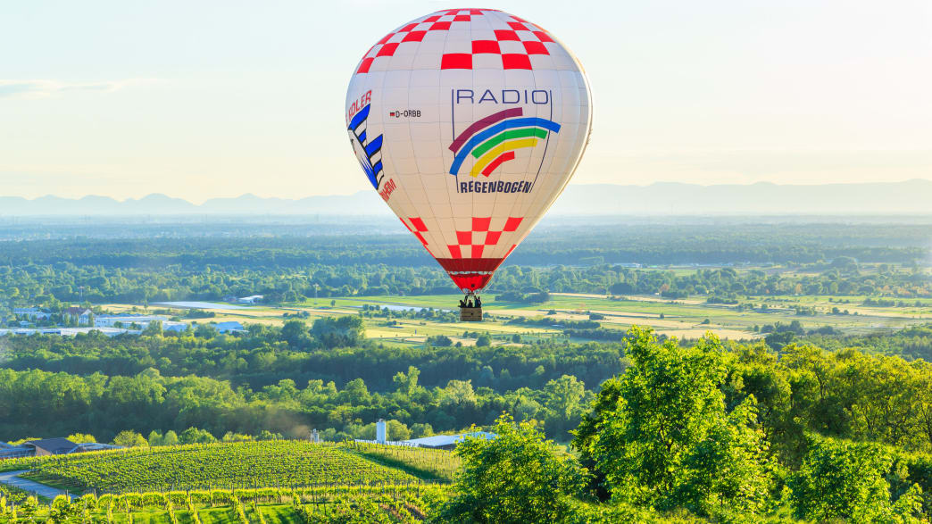Ein bunter Heißluftballon fliegt über eine Landschaft mit Weinbergen