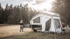 Eine Frau steht vor der Küchenzeile des Campwerk Economy Zeltanhängers auf einer Wiese im Wald