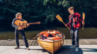 Peter Maffay mit Gitarre und Tim Bendzko mit Paddeln neben einem Kanu
