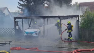 Ein Elektroauto verbrennt unter einem Carport und die Feuerwehr muss löschen