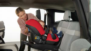 Junge Mutter befestigt den Kindersitz ihres Babys auf der Rückbank des Autos vorschriftsmäßig