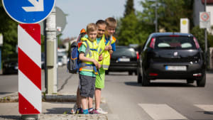 Schulkinder stehen an einem Zebrastreifen und schauen nach dem Verkehr