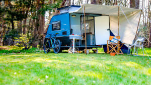 Ein helblauer Kip Shelter Wohnwagen mit Zeltdach und Fahrrad im Wald