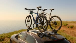 Fahrräder auf dem Dach des Autos am Rande des Berges vor dem Hintergrund des Meeres und des Sonnenuntergangs.