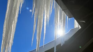 Lange Eiszapfen an einem Häuserdach glänzen im Sonnenlicht