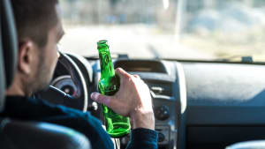 Mann trinkt Bier beim Autofahren