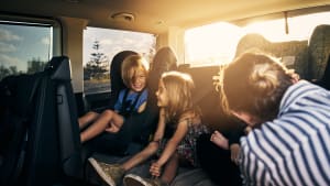 Mutter lacht mit drei Kindern auf der Rückbank eines Autos