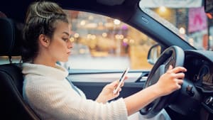 Frau schreibt während des Autofahrend auf ihrem Smartphone