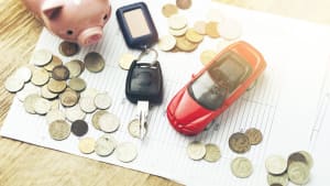Münzen, Autoschlüssel, Sparschwein und Spielzeugauto auf einem Tisch