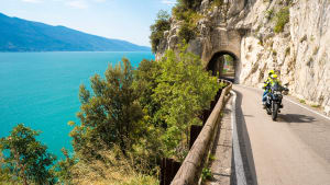 Ein Motorradfahrer mit Sozius fährt am Gardasee vorbei