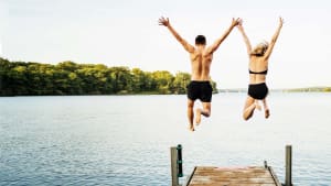 Mann und Frau springen von einem Steg aus in einen See