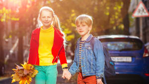 Ein Mädchen und ein Junge überqueren an einem sonnigen Herbststag sicher die Srraße