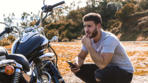 Mann kniet mit seinem Handy neben seinem Motorrad mit Panne