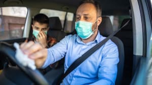 Autofahrer trägt Mundschutz und reinigt Lenkrad