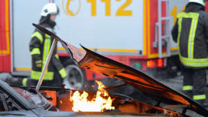 De Feuerwehr steht nach einem Unfall hinter einem brennenden Autoauf einer Straße