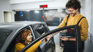 Frau im Auto übergibt Automechaniker den Autoschlüssel