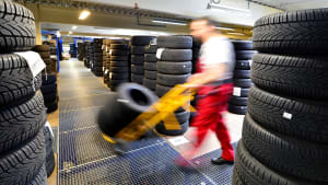 Ein Mitarbeiter eines Reifenhändlers fährt mit Sackkarre an aufgetürmten Reifen vorbei