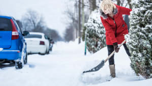 Frau nräumt Schnee vor Ihrem Wohnhaus