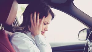 Frau hat Stress im Auto und hält sich die Ohren zu