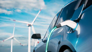 Ein Elektroauto wird geladen, im Hintergrund sind Windkrafträder und blauer Himmel zu sehen