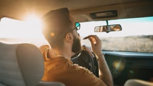 Mann kämmt sich den Bart am Steuer eines Autos bei der Fahrt im Sonnenaufgang