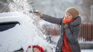 Frau kratzt Schnee und Eis von ihrem Auto