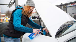 Eine rothaarige Frau fuellt Reinigungsflüssgkeit in die Scheibenwischanlage Ihres Autos
