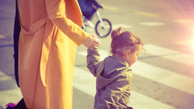 Kleines Mädchen überquert die Straße an der Hand ihrer Mutter