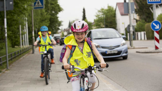 Ein Mädchen mit Fahrrad, Helm und Warneste im Strassenverkehr