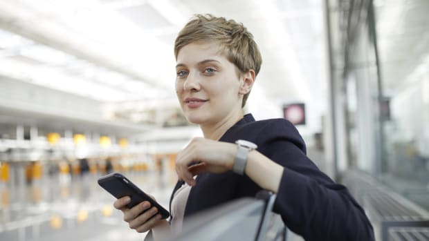Eine Frau sitzt mit einem Handy in einer Halle am Flughafen
