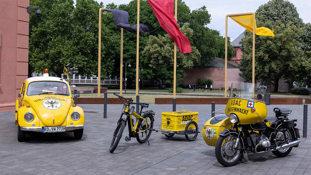 Historische Fahrzeuge der ADAC Straßenwacht. VW Käfer, Fahrrad mit Anhänger und Motorradgespann.