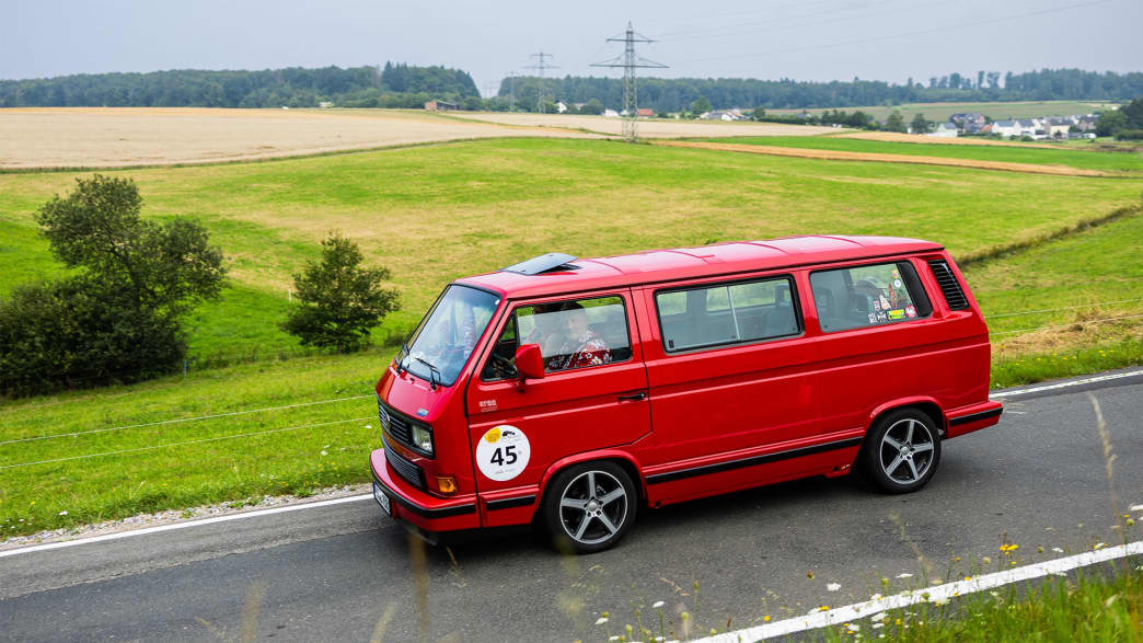 VW Multivan Last Limited Edition, Baujahr 1992: Dieser leuchtend rote Multivan fährt durch eine malerische Landschaft und zeigt den ikonischen Stil und die Vielseitigkeit dieses klassischen VW-Modells.