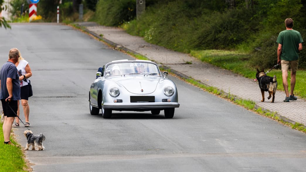 Dieser silberne Porsche verkörpert den klassischen Stil und die sportliche Eleganz der 50er Jahre und fährt durch eine idyllische Dorfstraße.
