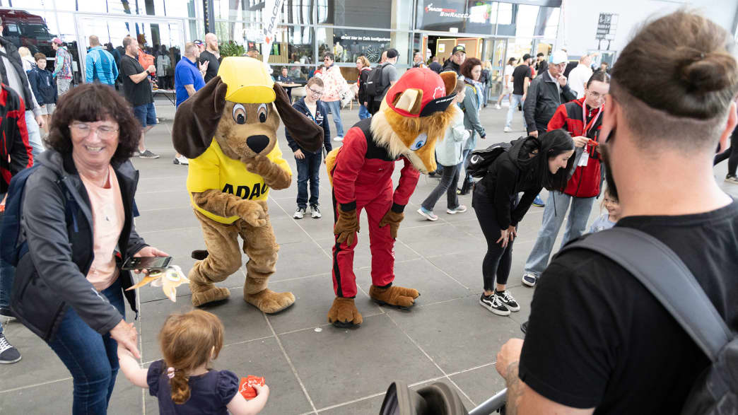 Familienfreundliche Veranstaltung, bei der Menschen mit Maskottchen interagieren, darunter ein Hund in einem gelben Outfit und ein Fuchs in einem roten Anzug.