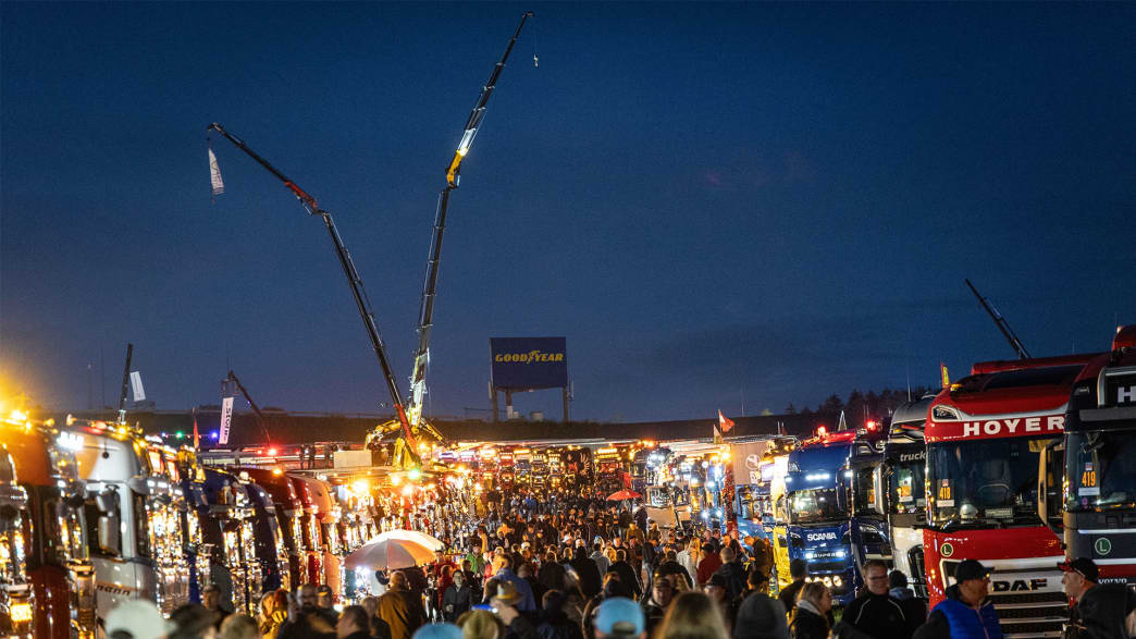 Nachtveranstaltung mit einer Menschenmenge, die die beleuchtete Ausstellung von Trucks und Aktivitäten genießt, hervorgehoben durch Kranlichter im Hintergrund.