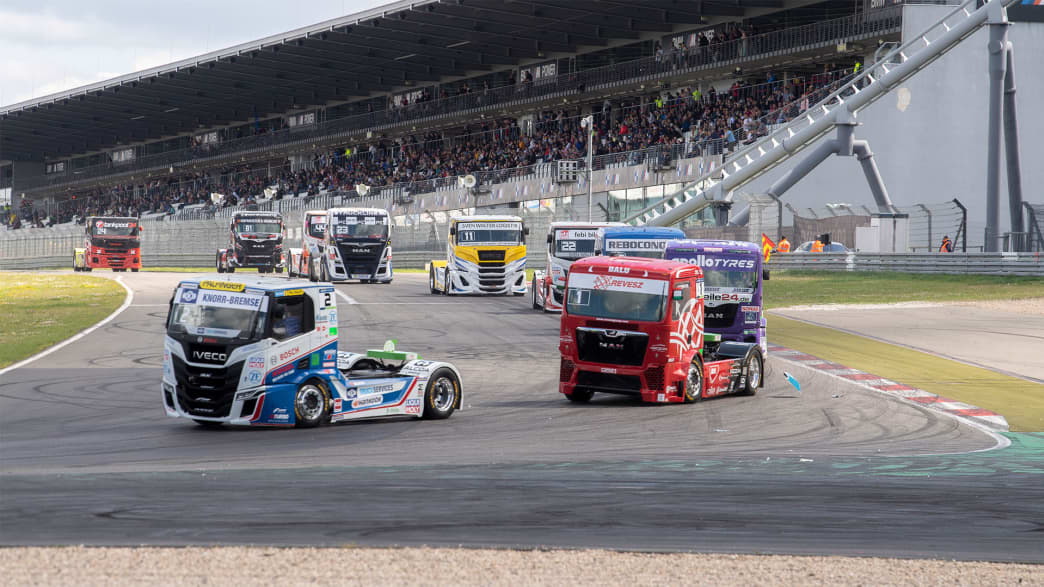 Truck-Rennen mit mehreren Trucks, die auf einer Rennstrecke konkurrieren, beobachtet von einer begeisterten Menge auf den Tribünen.