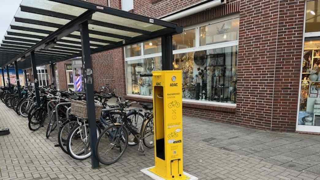 Eine gelbe Säule steht vor einem überdachten Fahrradständer. Im Hintergrund ist ein Geschäft in der Fußgängerzone zu sehen.