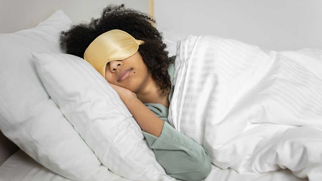 Eine Frau liegt mit einer goldenen Schlafmaske im Bett und schläft.