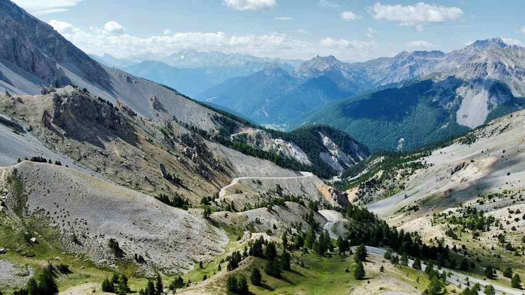 Blick nach Süden vom Col d’Izoard auf eine kurvige Straße und grüne alpine Landschaft in den französischen Seealpen.