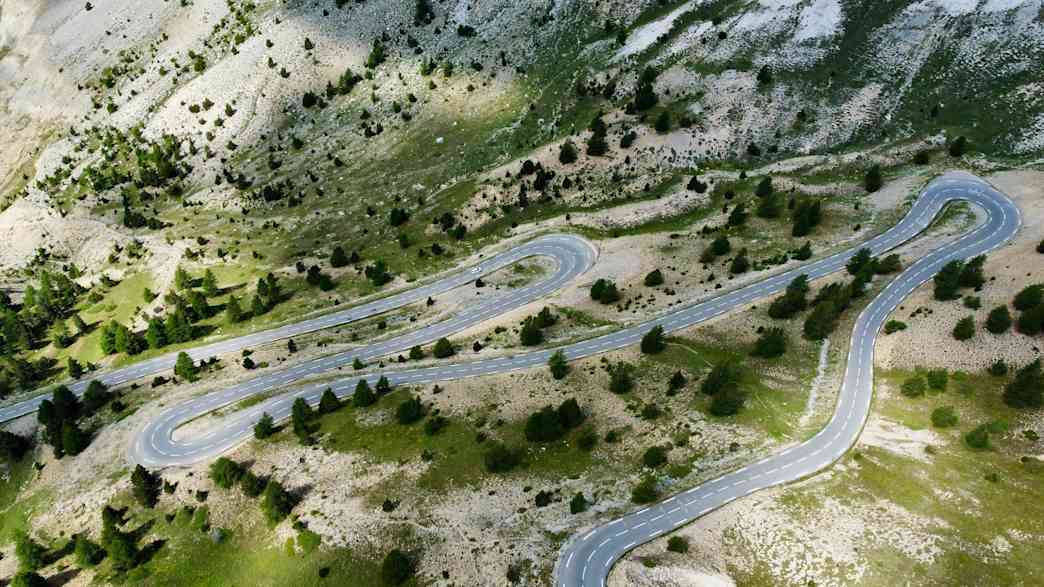 Serpentinenstraße am Col d’Izoard in den französischen Seealpen, umgeben von Felsen und grüner Vegetation.