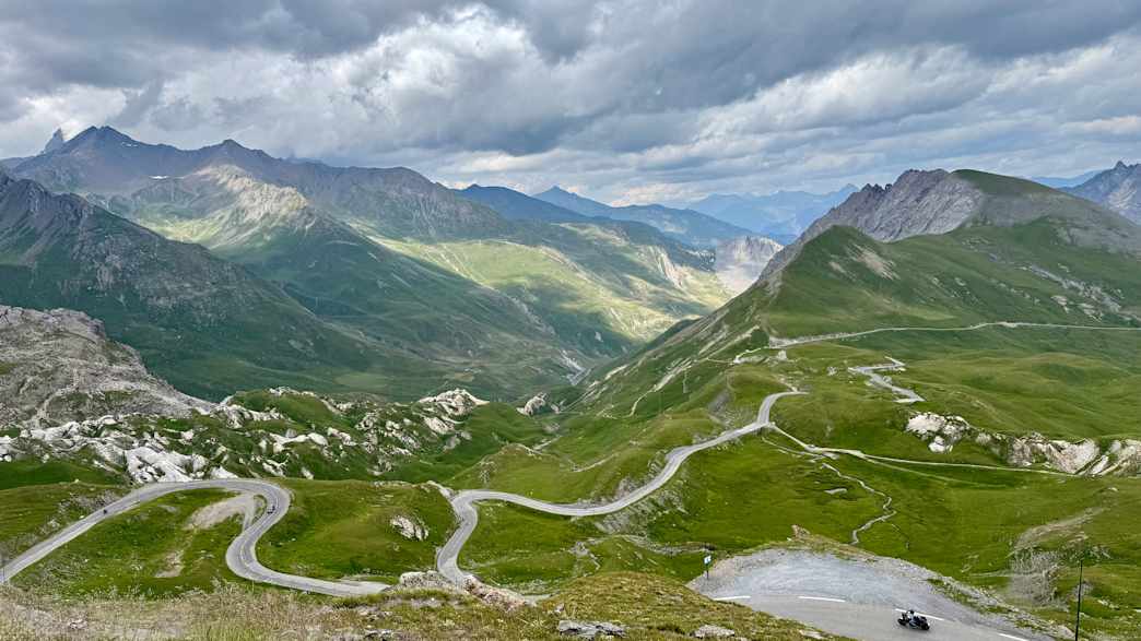 Serpentinenstraße am Col du Galibier in den französischen Seealpen mit grünen Tälern und bewölktem Himmel.