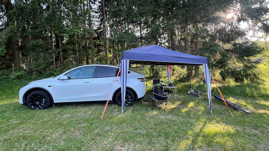 Ein Tesla Model Y steht auf einer Wiese, hinter ihm ist ein kleiner Pavillon aufgebaut mit Fahrrädern
